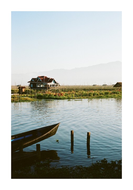 A boat is docked on a lake with a house on stilts and mountains in the background.