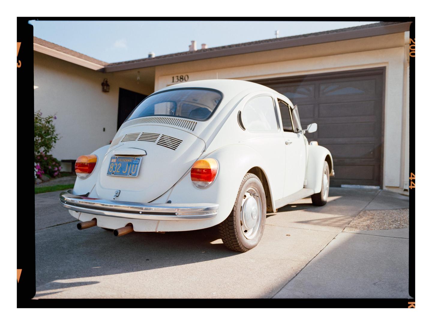 A white Volkswagen Beetle is parked in a driveway in front of a garage.