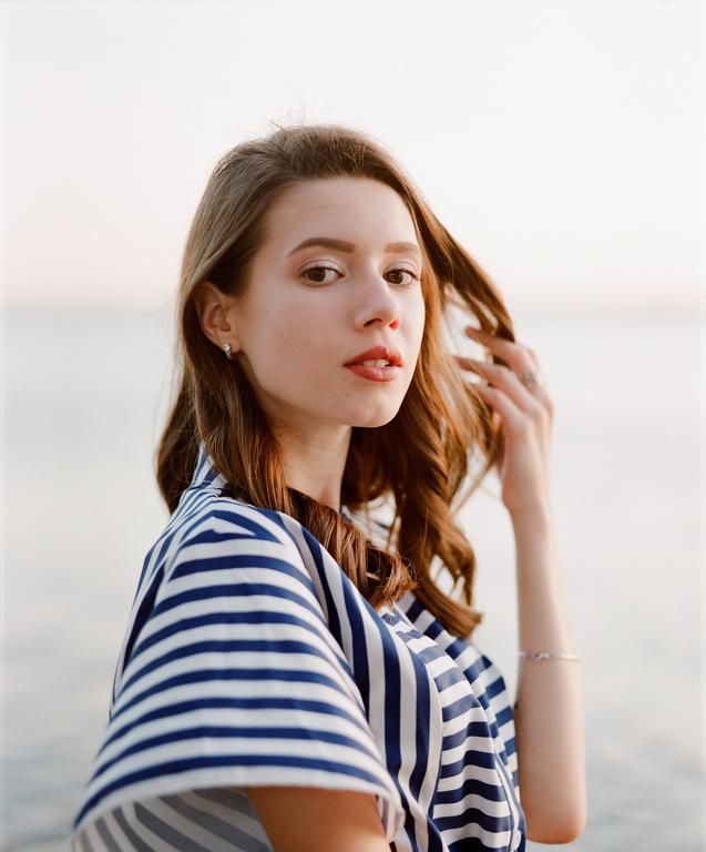 A woman with long brown hair and a striped shirt looks directly at the viewer.