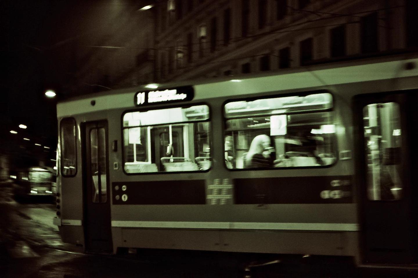 A tram moves through a city street at night, with a person visible through a window.
