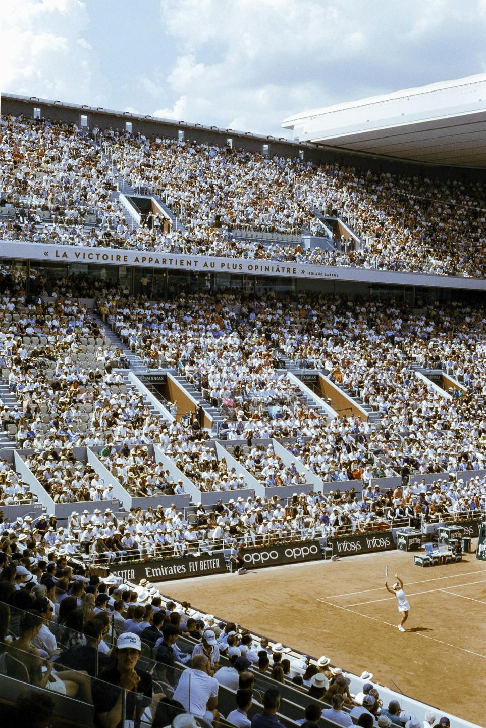 A tennis player serves on a clay court in a stadium filled with spectators.