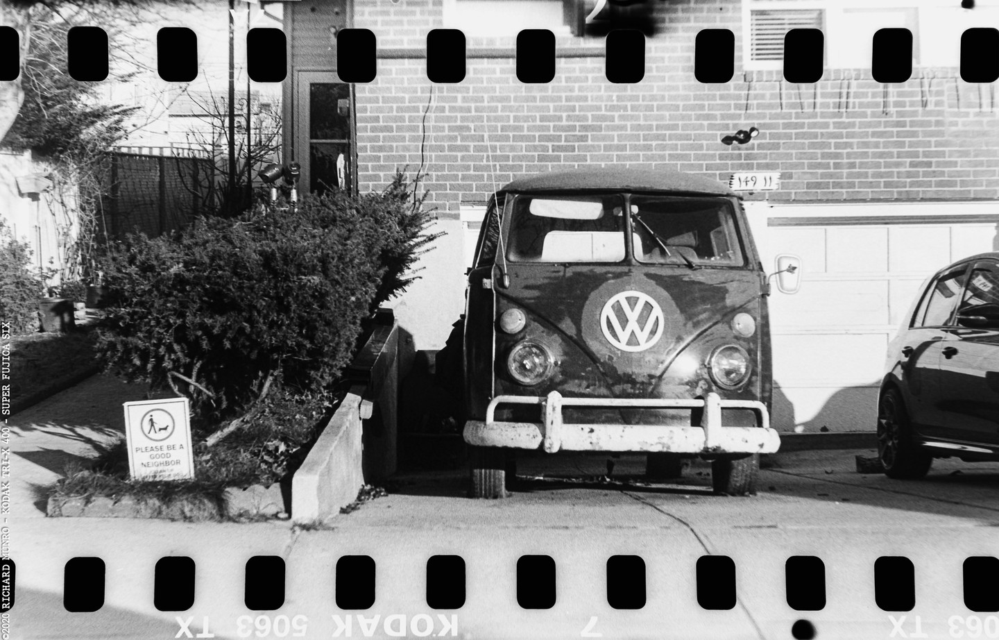 A Volkswagen van is parked in a driveway next to a brick house and a garage.