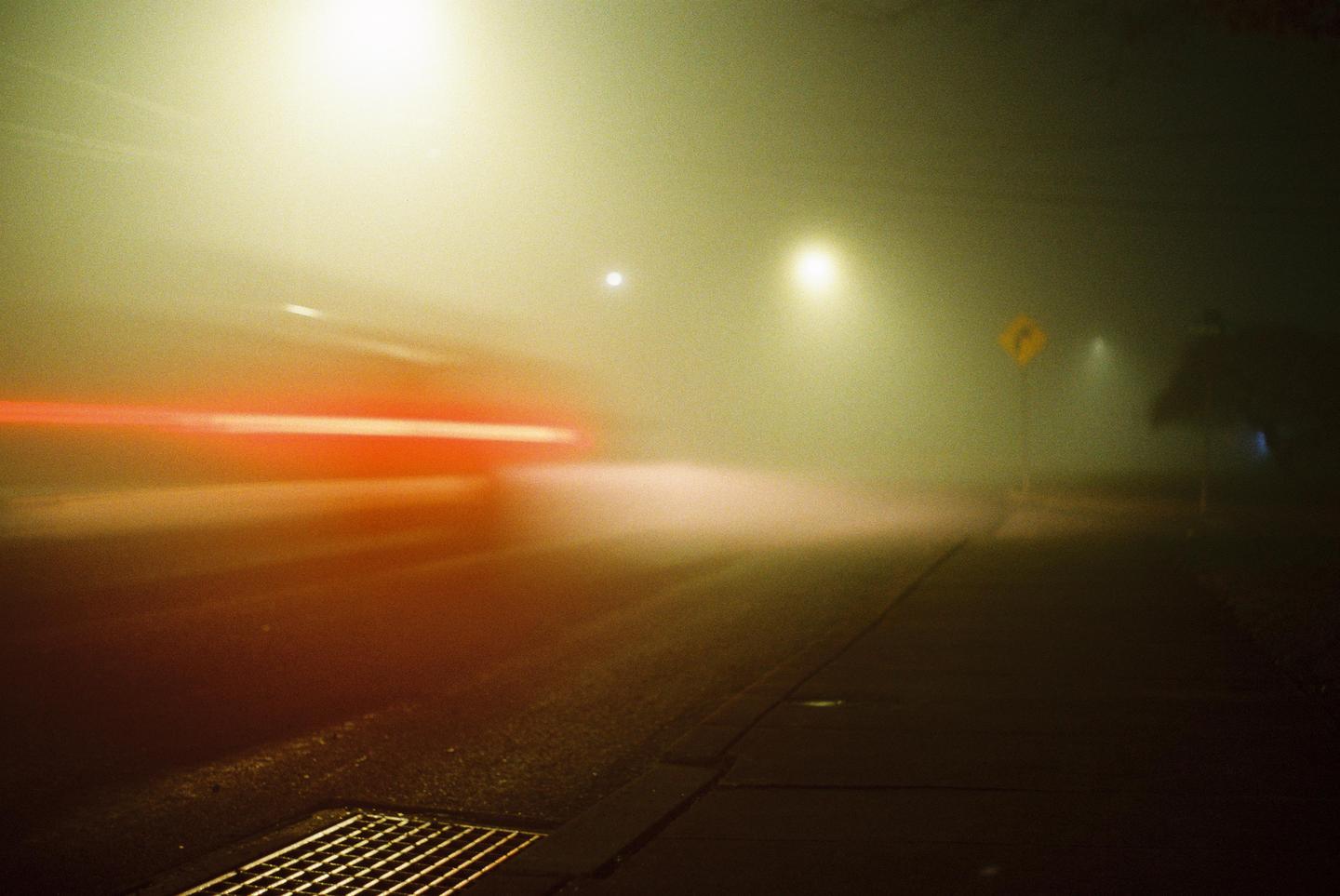 A street at night is illuminated by streetlights and the red light trails of a passing vehicle.
