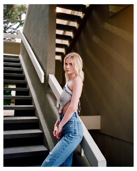 A woman stands on a concrete staircase with a railing, looking towards the viewer.