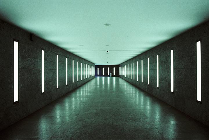 A long, empty subway tunnel is illuminated by vertical fluorescent lights on both walls.