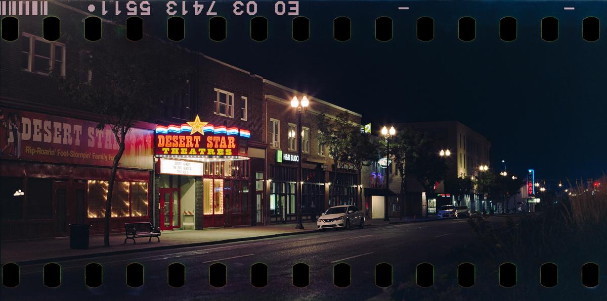A street at night is illuminated by the neon sign of the Desert Star Theatre and streetlights.