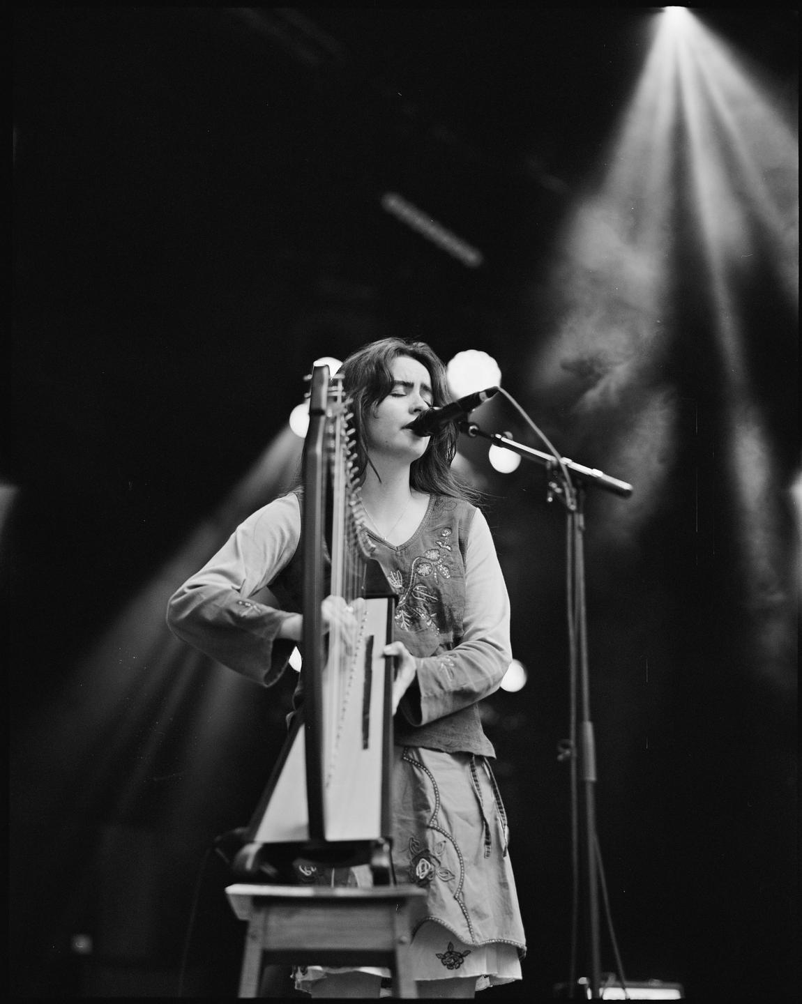 A woman sings into a microphone while playing a harp on a stage with spotlights.