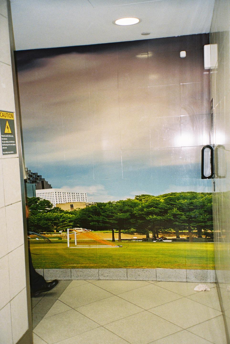 A person stands next to a glass door with a large image of a park and city buildings printed on it.