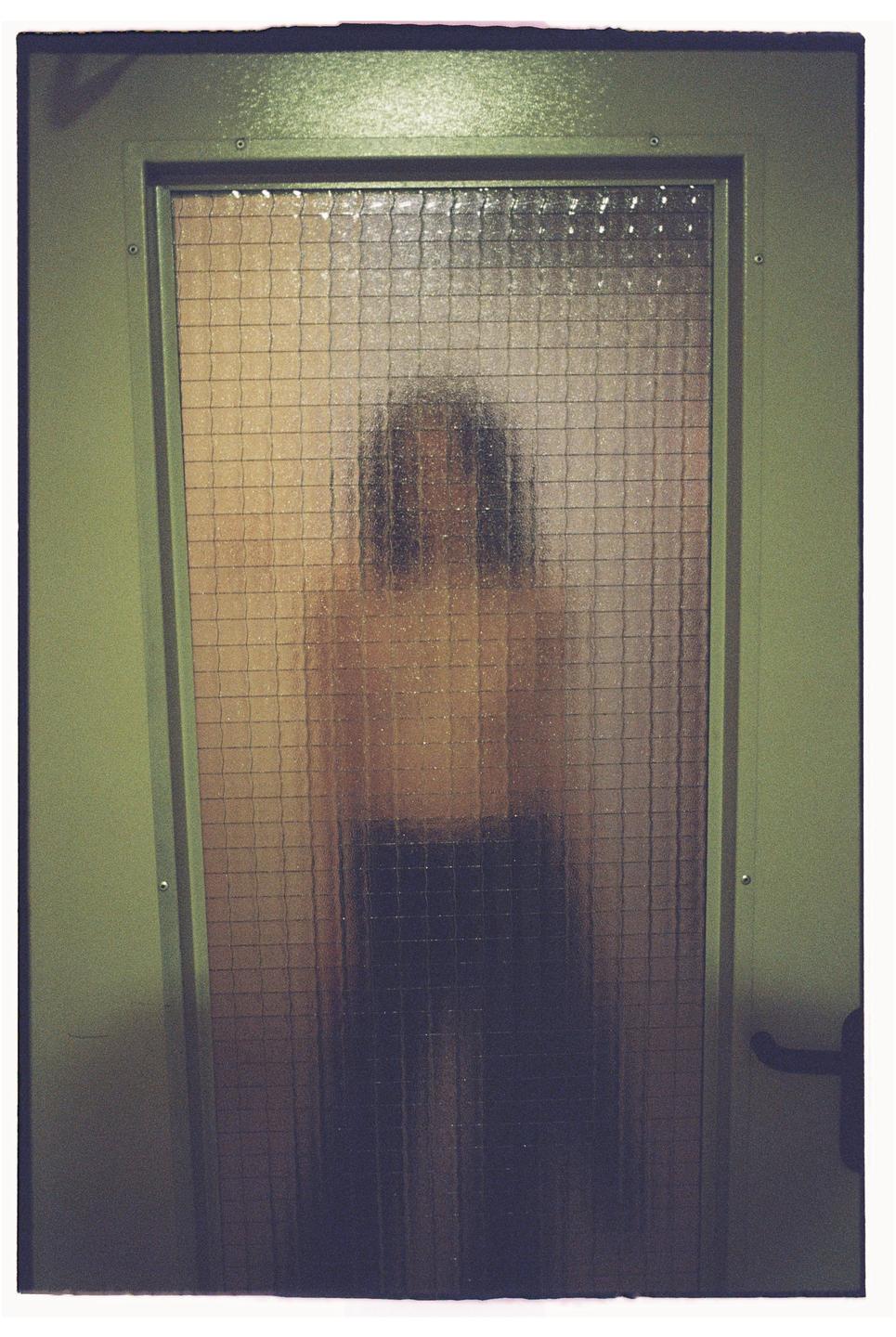 A person is visible through a textured glass door.