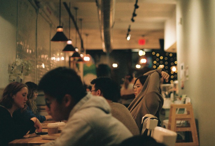 People are sitting at tables in a restaurant at night with bokeh lights in the background.