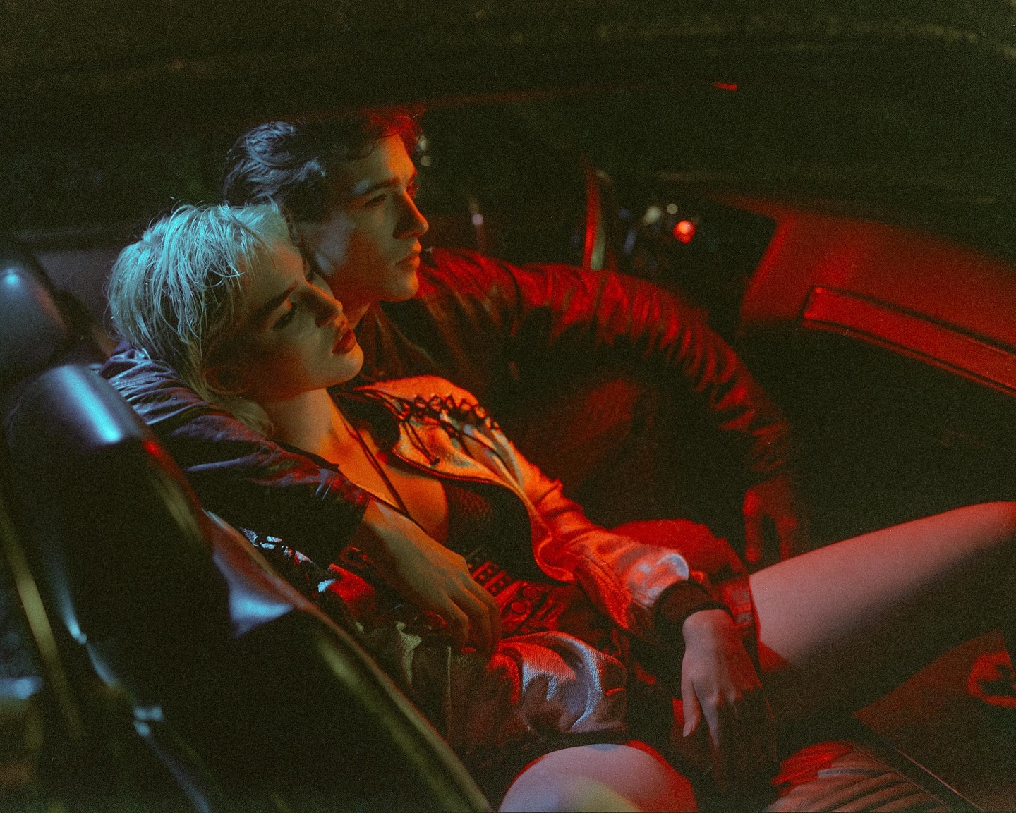 A couple sits in a car at night, illuminated by red and blue light.