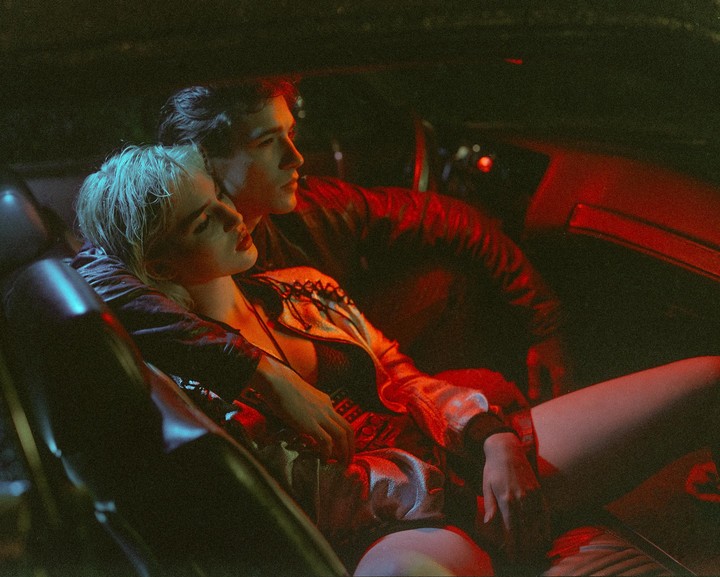 A couple sits in a car at night, illuminated by red and blue light.