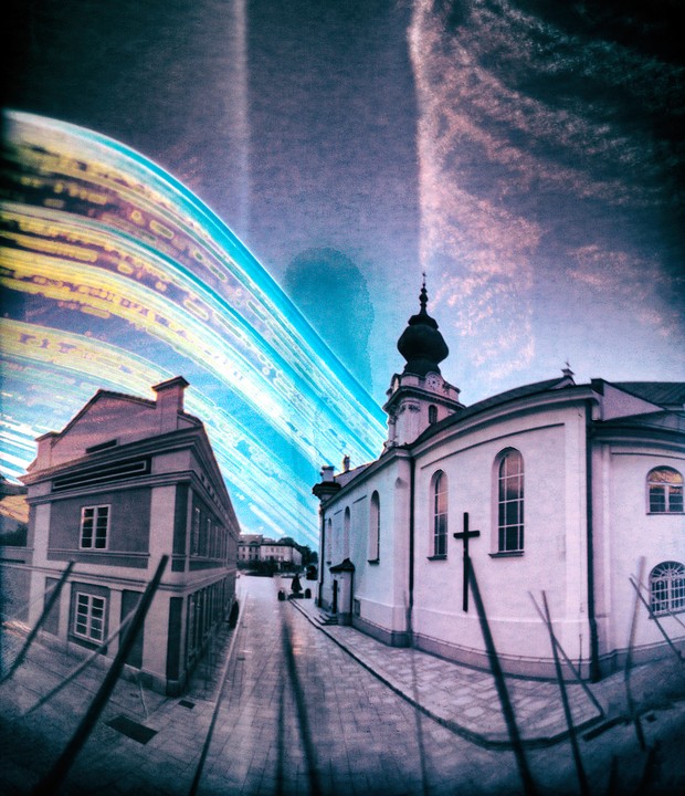 A street with a church and another building is visible under a sky with light trails.