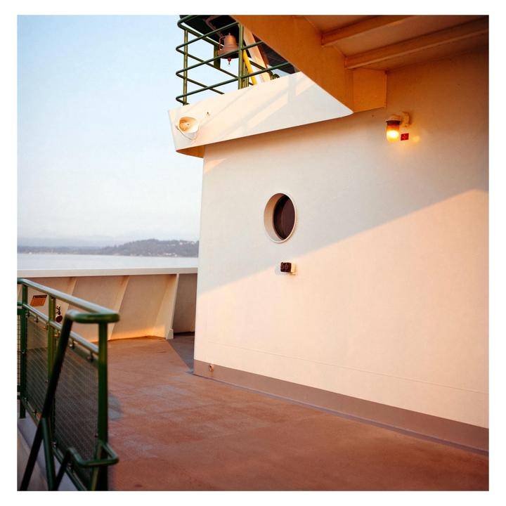 A ferry deck with a porthole and a light is illuminated by the sun.