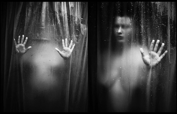 A person is visible behind a wet shower curtain with their hands pressed against it.