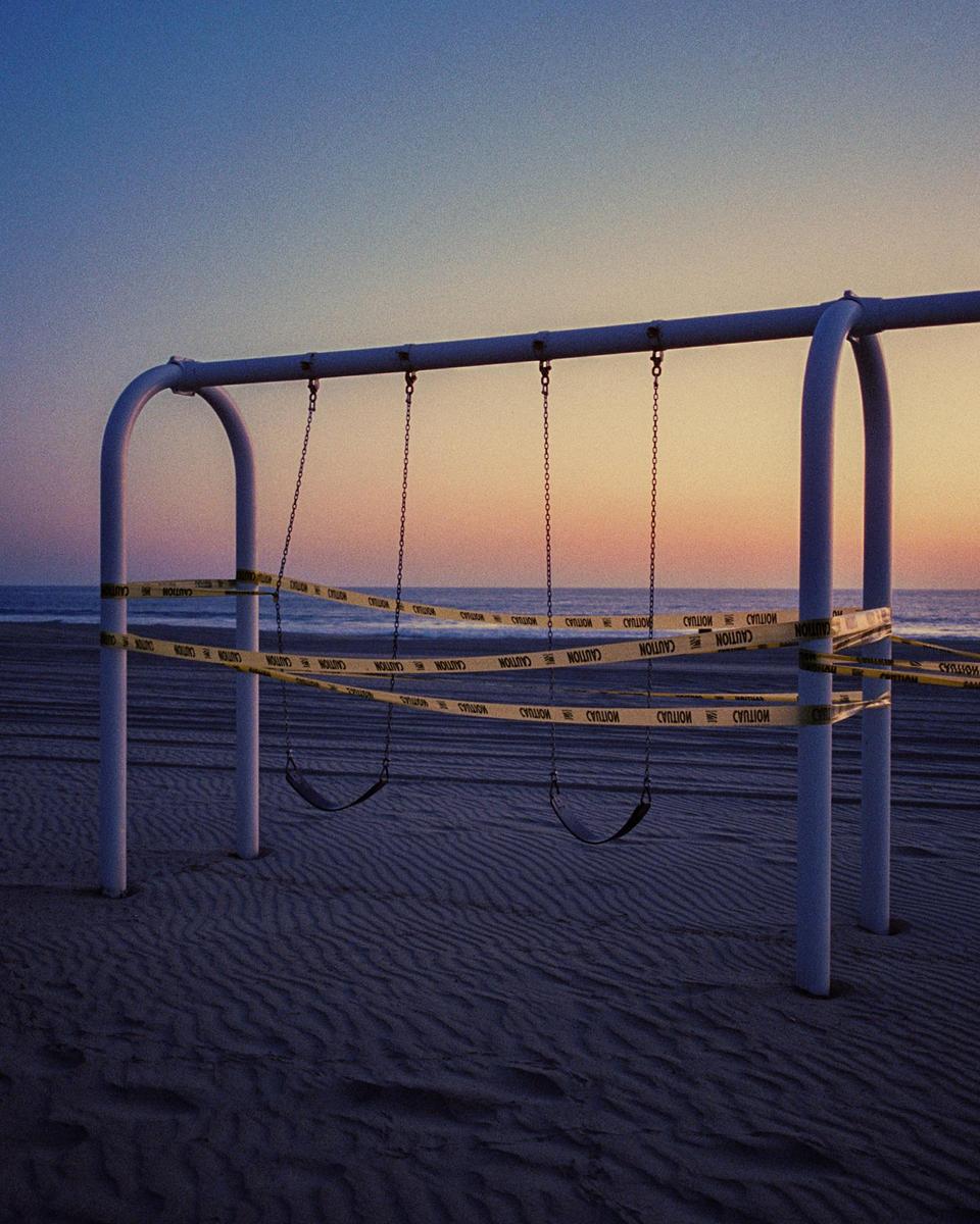 A swing set on a sandy beach is wrapped with caution tape at sunset.