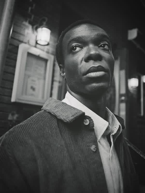 A man in a corduroy jacket and collared shirt looks up and to the right.
