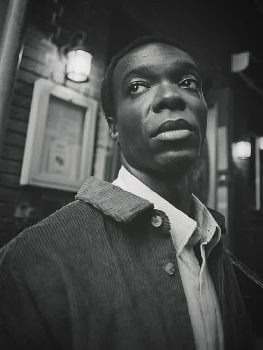 A man in a corduroy jacket and collared shirt looks up and to the right.