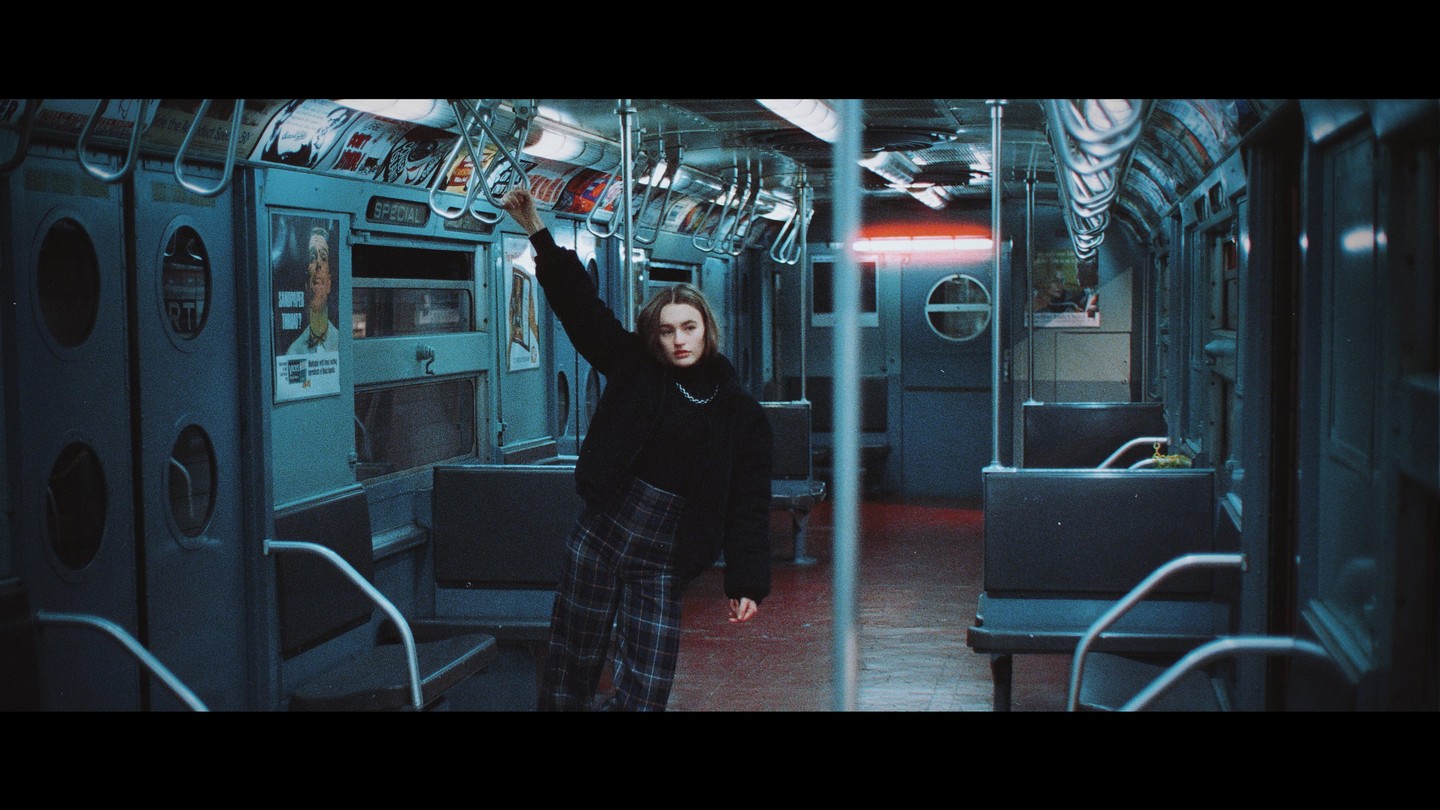 A woman stands in an empty subway car, holding onto a handrail.