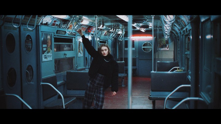 A woman stands in an empty subway car, holding onto a handrail.