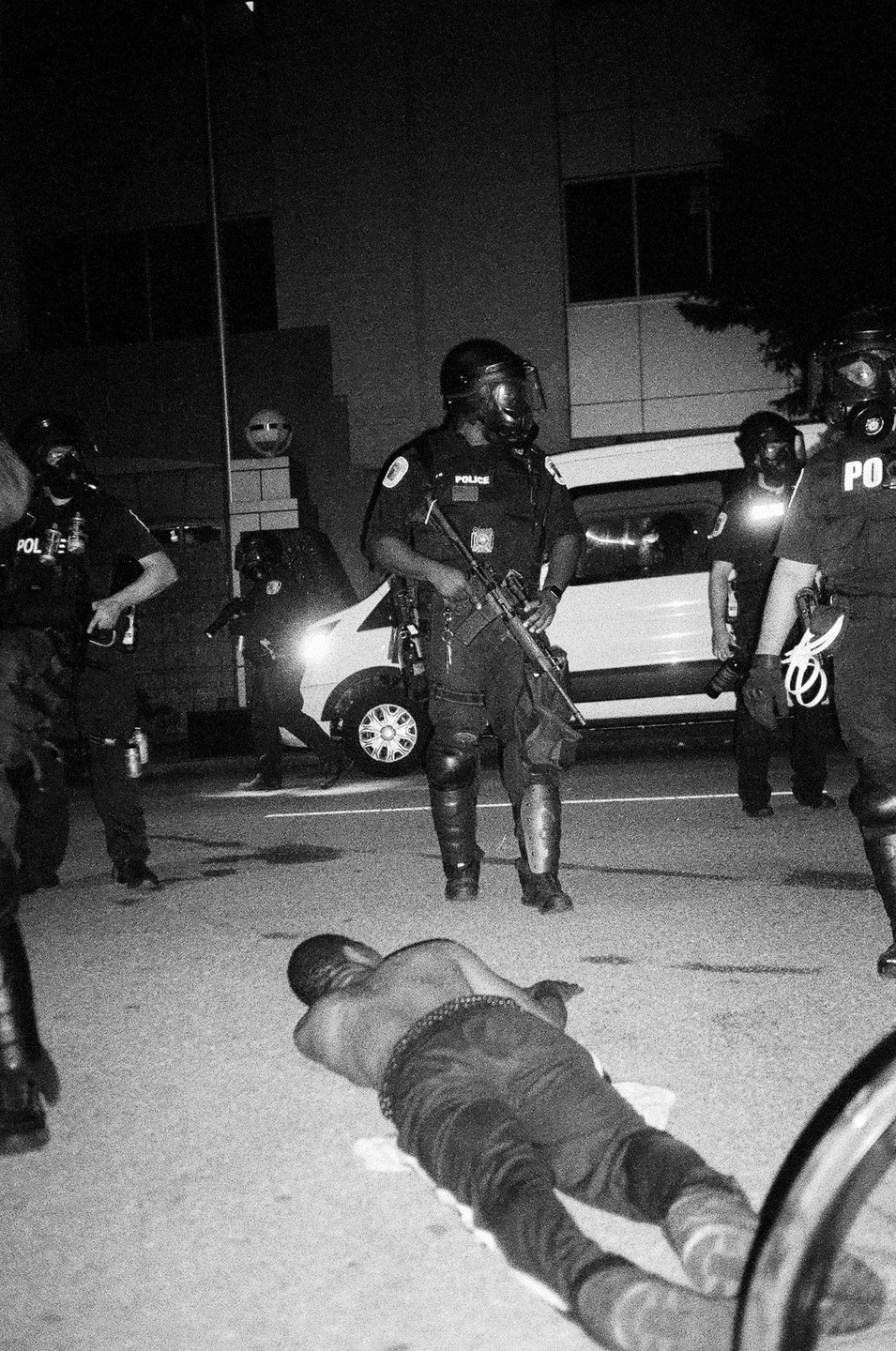 A man lies on the ground in front of several police officers and a police van at night.
