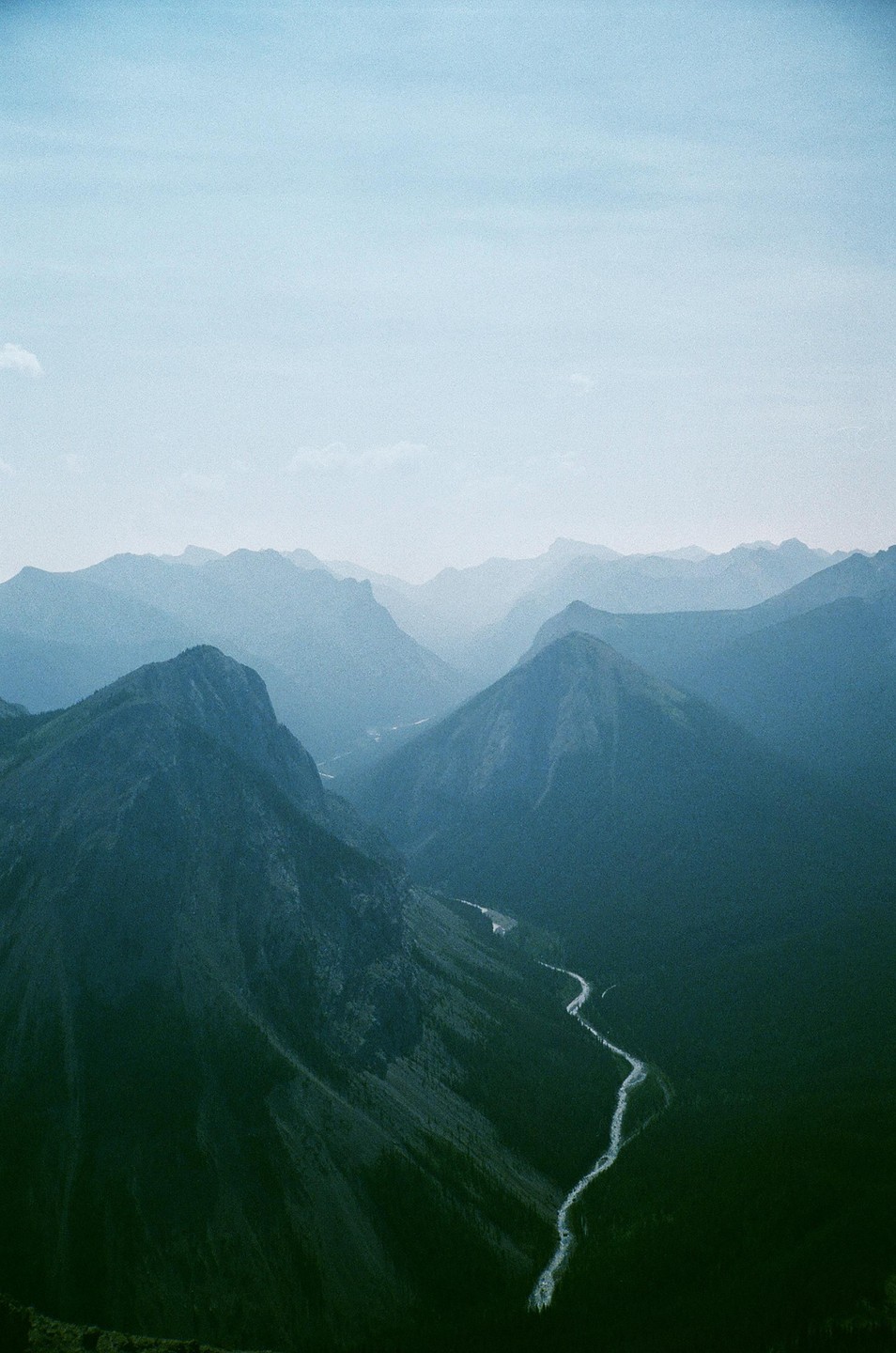 A winding river flows through a valley surrounded by mountains under a hazy sky.