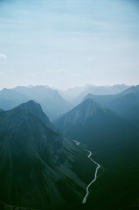 A winding river flows through a valley surrounded by mountains under a hazy sky.