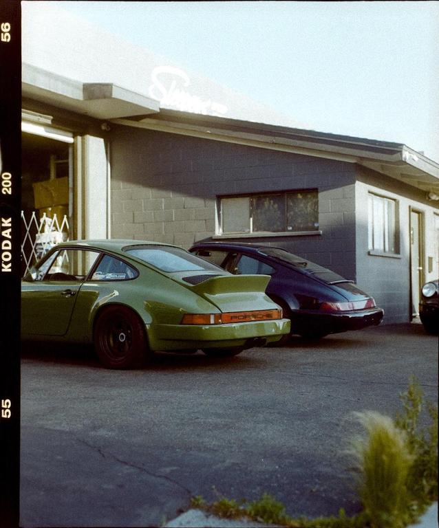 Two Porsche cars are parked outside a building with a light blue sky overhead.
