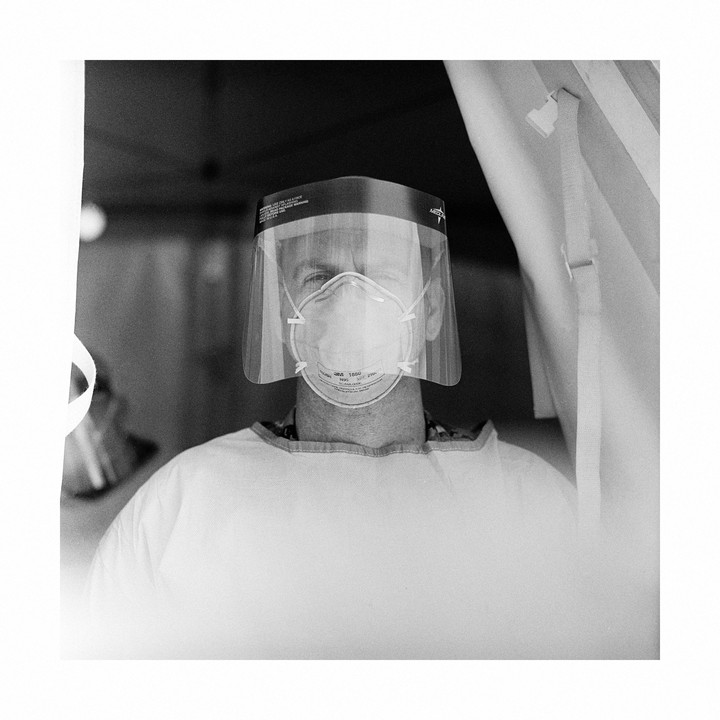 A man wearing a face shield and mask is visible in a black and white portrait.