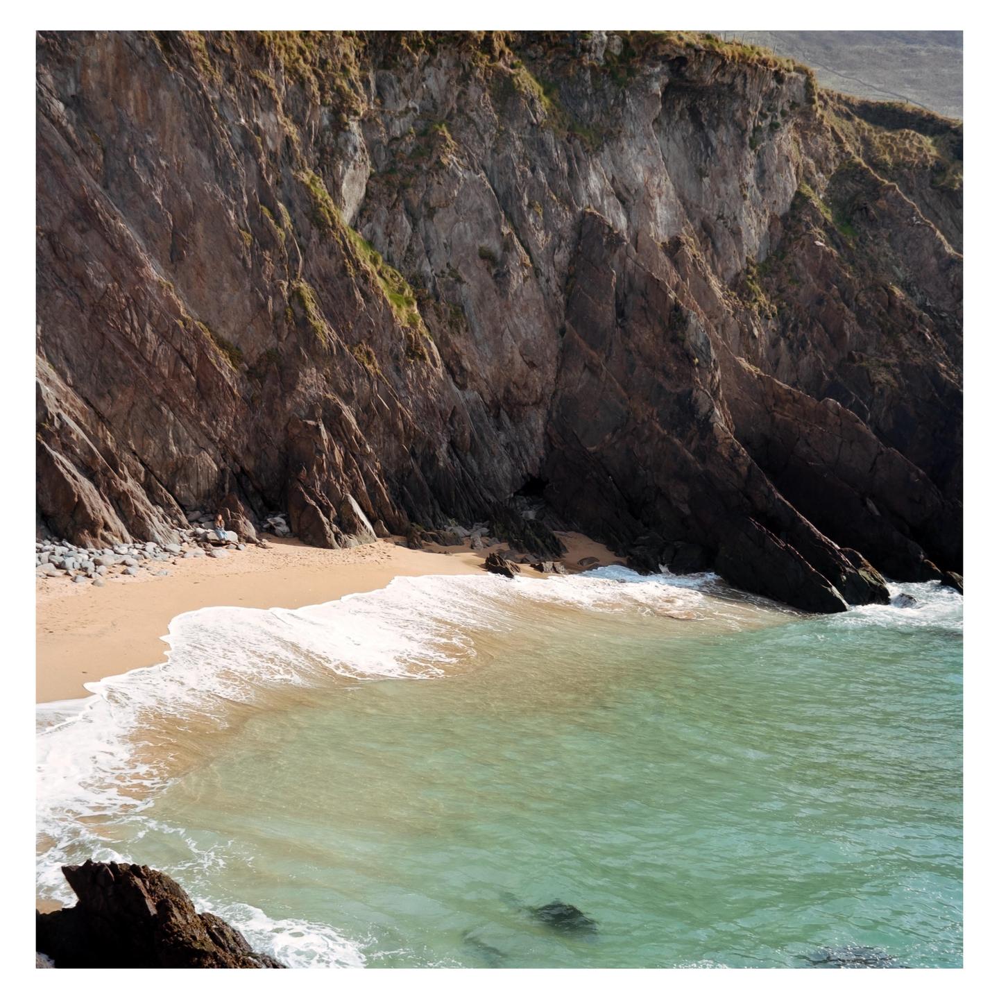 A small beach with turquoise water is nestled at the base of a tall, rocky cliff.