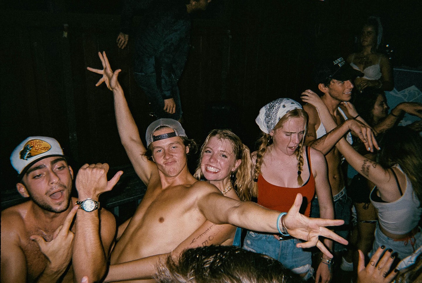 A group of young people are dancing and posing for the camera in a dark setting.
