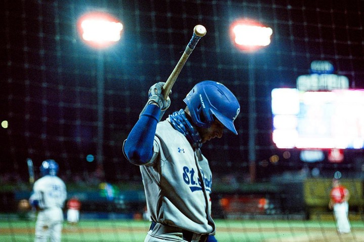 A baseball player in a blue helmet and gray uniform holds a bat on a field at night.