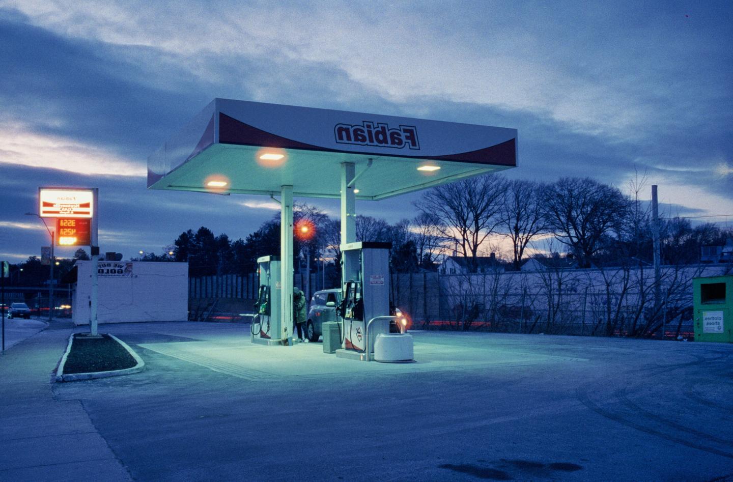 A person fills a car with gasoline at a gas station at dusk.