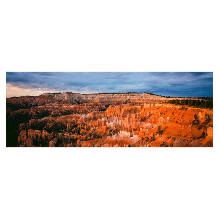 A panoramic landscape shows the orange and white rock formations of Bryce Canyon under a cloudy sky.