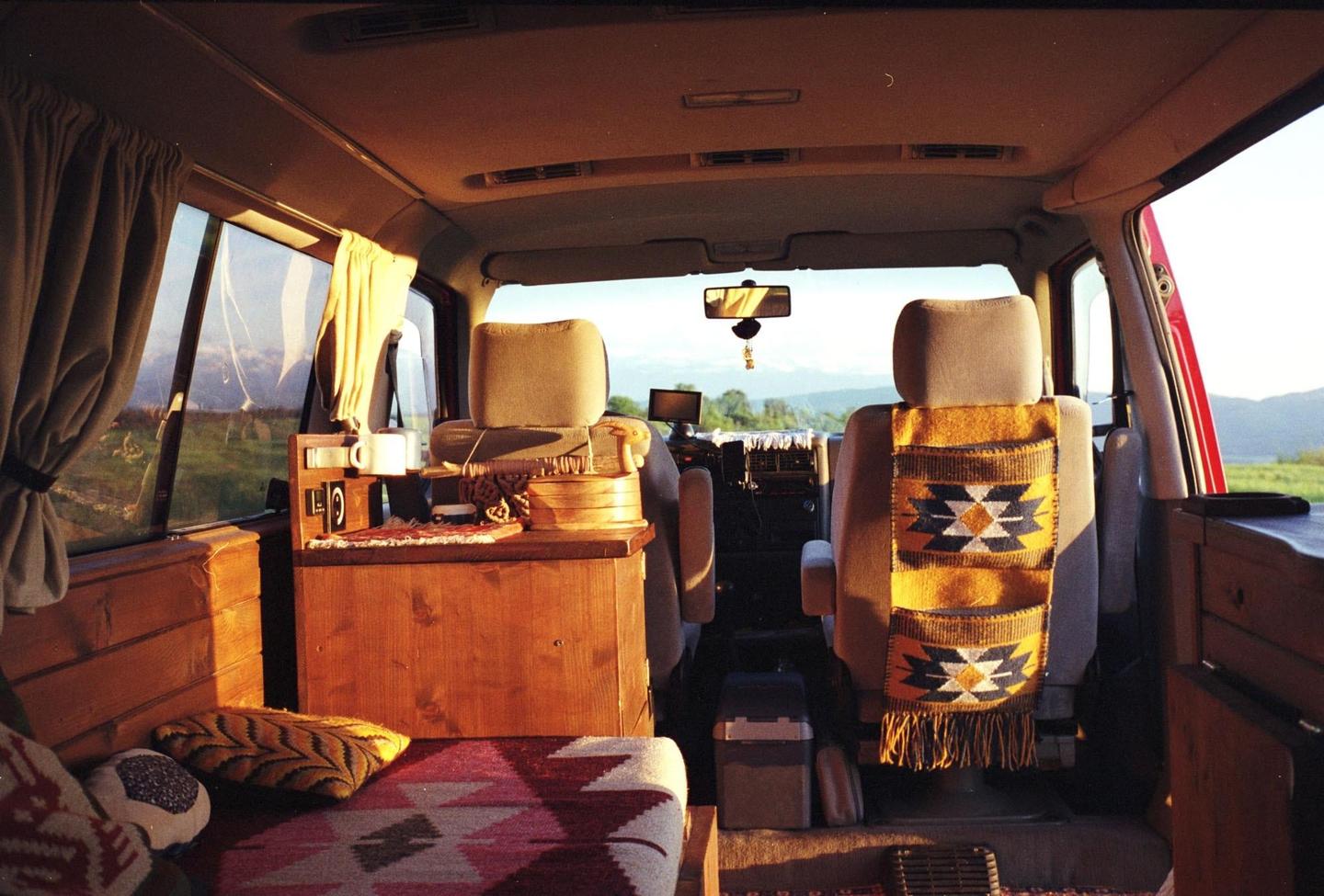 The interior of a camper van is visible with a view of a green landscape through the windows.