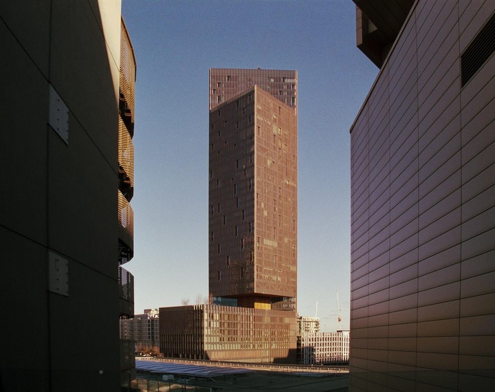 A tall, brown, rectangular building stands between two other buildings, with a clear sky above.
