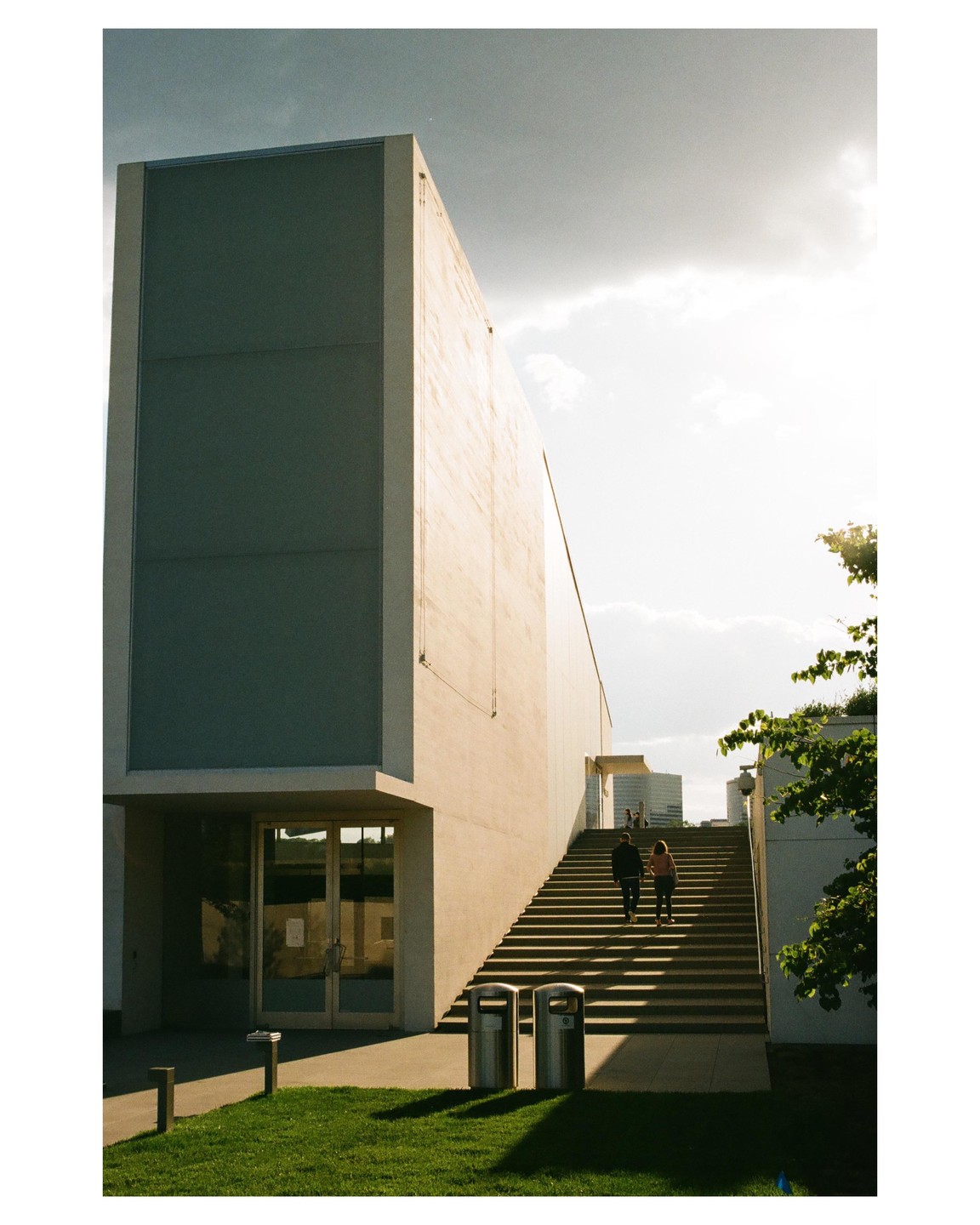 A couple walks up a long outdoor staircase next to a modern building with a bright sky overhead.