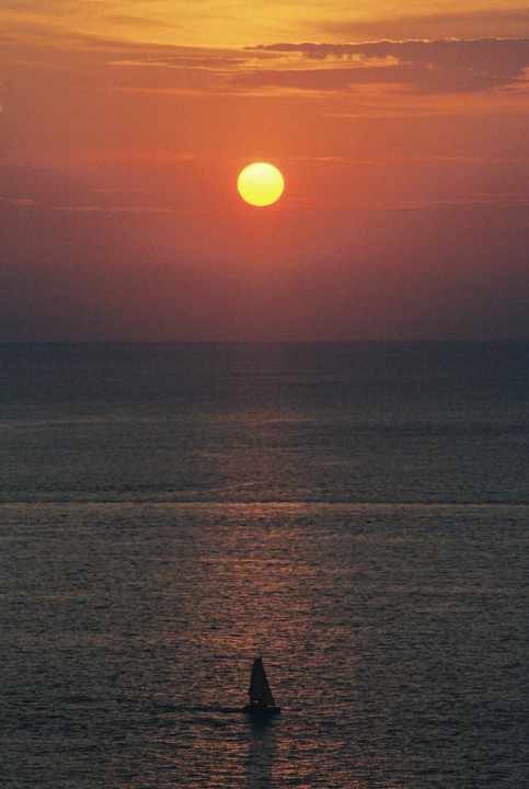 A sailboat is silhouetted against the ocean at sunset.