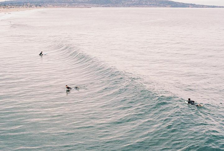 Three surfers are in the ocean with a large wave approaching the shore.