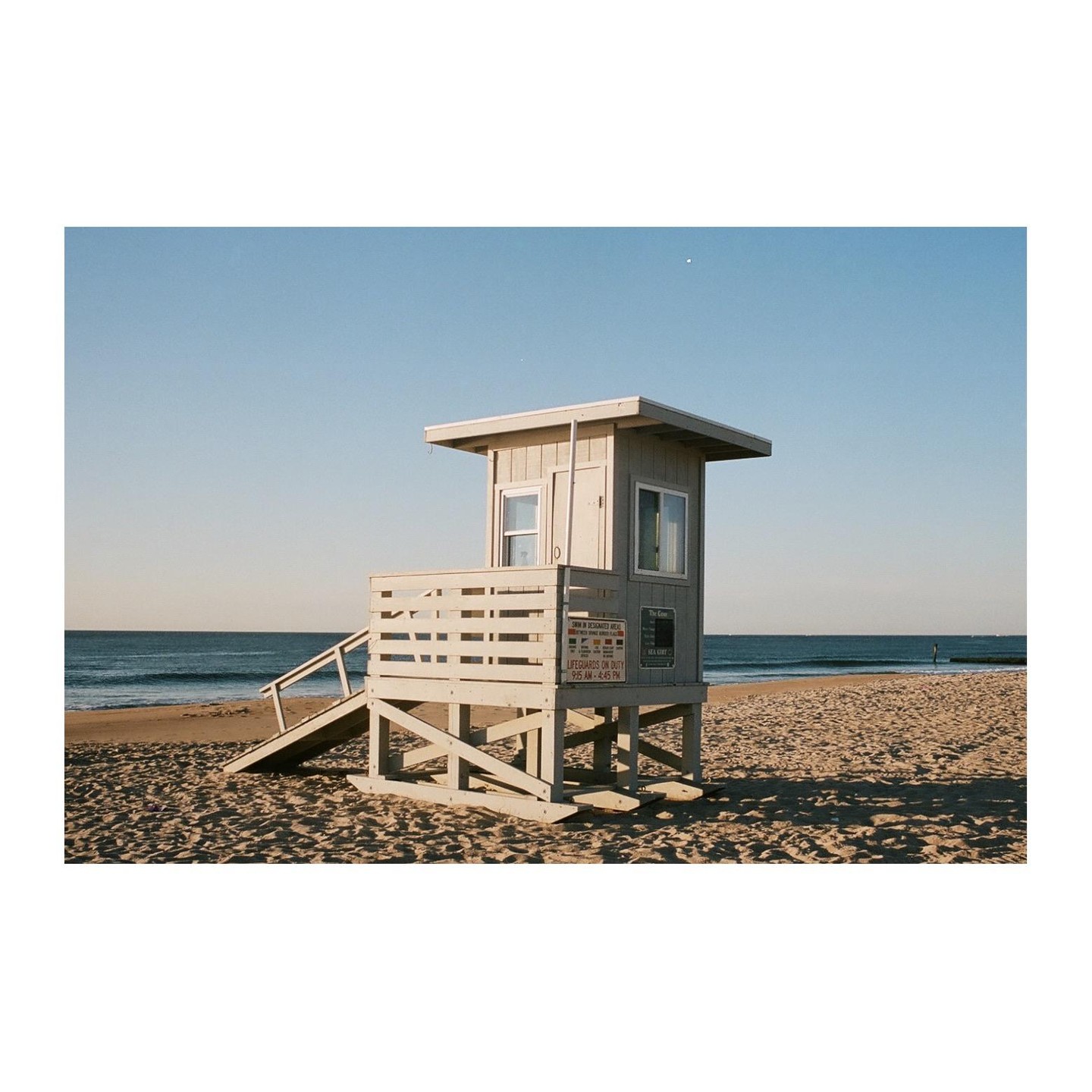 A lifeguard stand sits on a sandy beach next to the ocean under a clear sky.