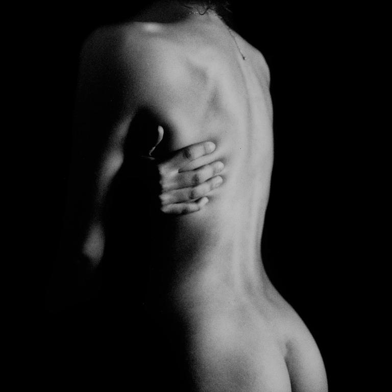 A woman's back is visible as she holds her arm across her body in a black and white portrait.