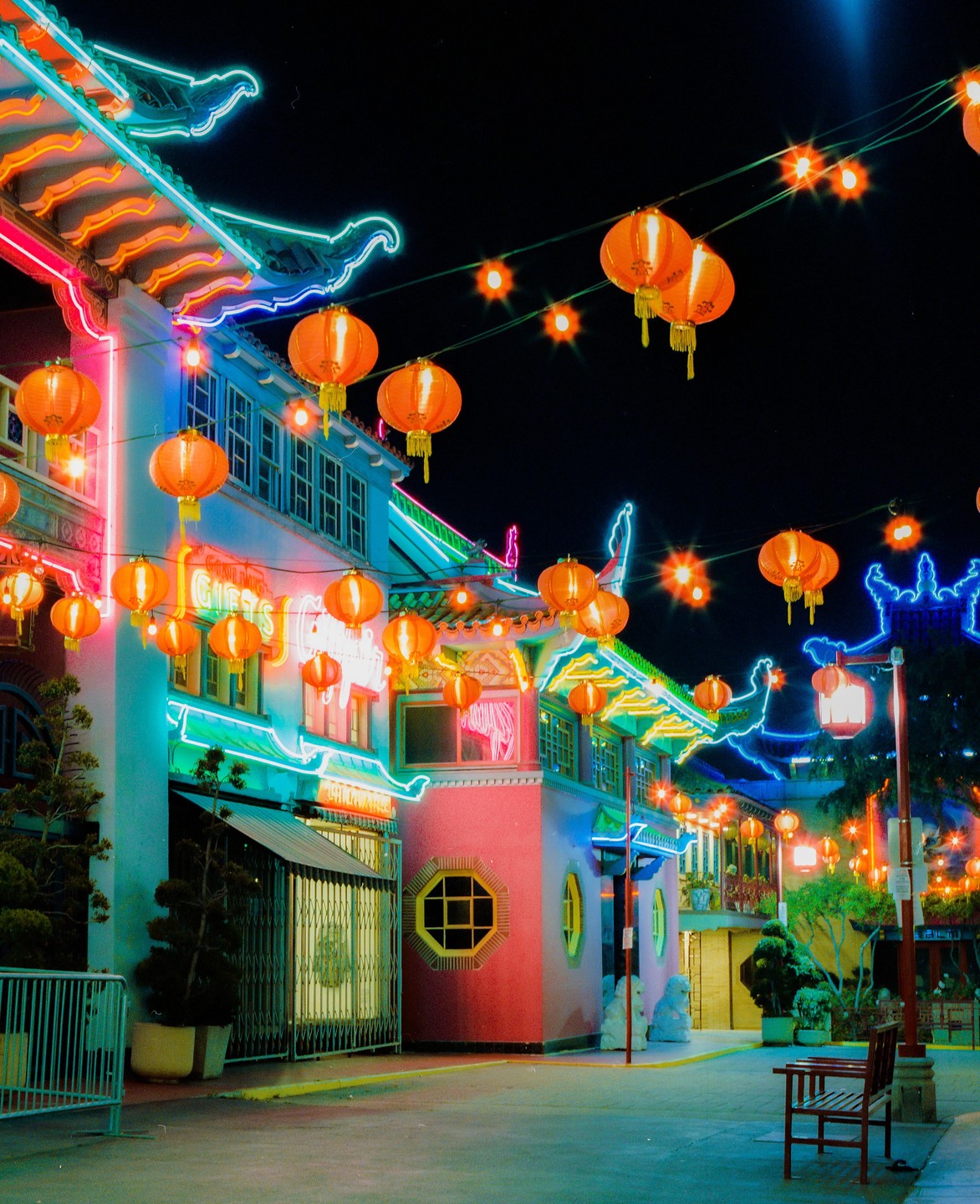 A street in Chinatown is illuminated by neon lights and many orange lanterns at night.
