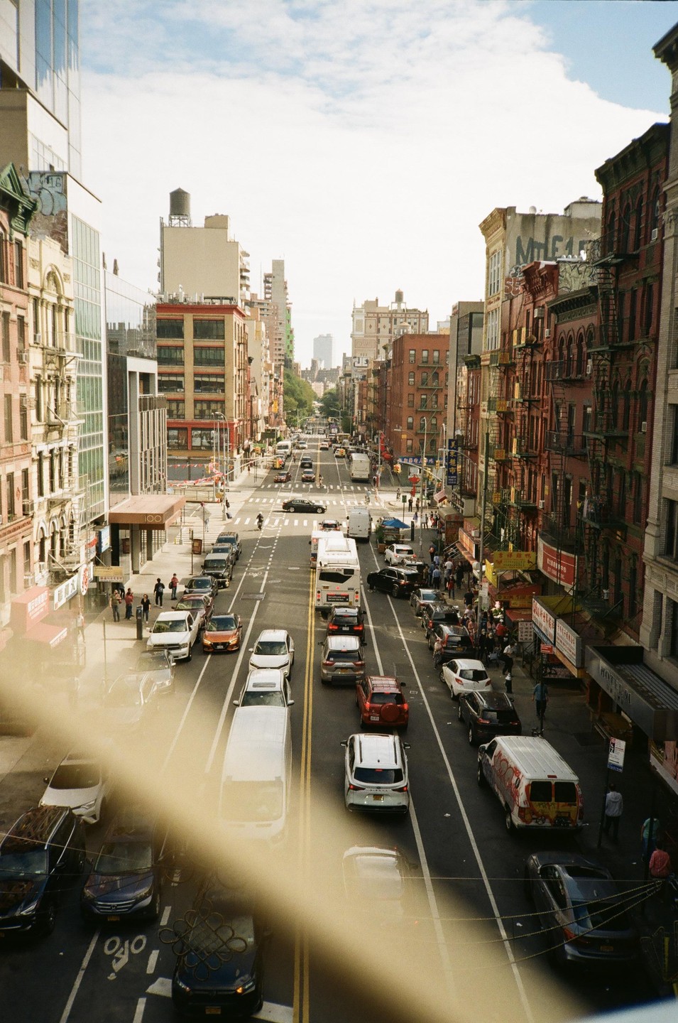 A busy street in New York City is filled with cars and pedestrians, with tall buildings lining both sides.