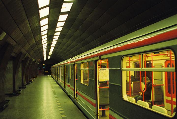 A subway train with open doors is stopped at a station platform with a person visible inside one of the cars.