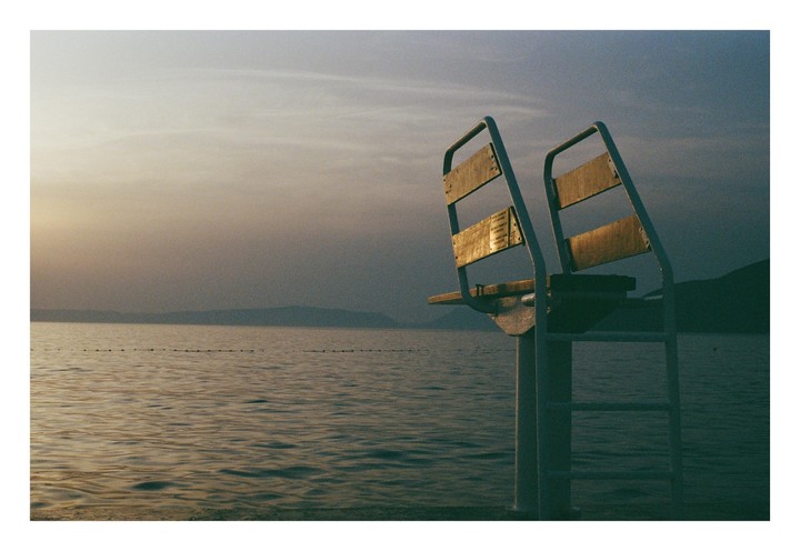 A diving platform stands at the edge of a calm body of water with mountains in the distance under a hazy sky.
