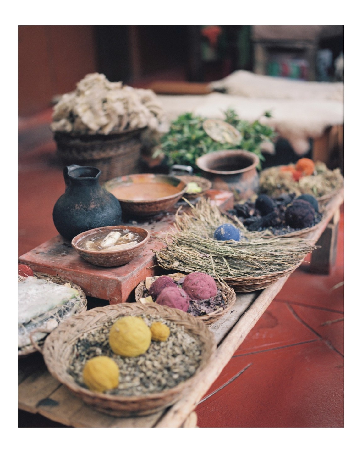 A table is laden with various natural dyes, yarns, and ingredients in bowls and baskets.