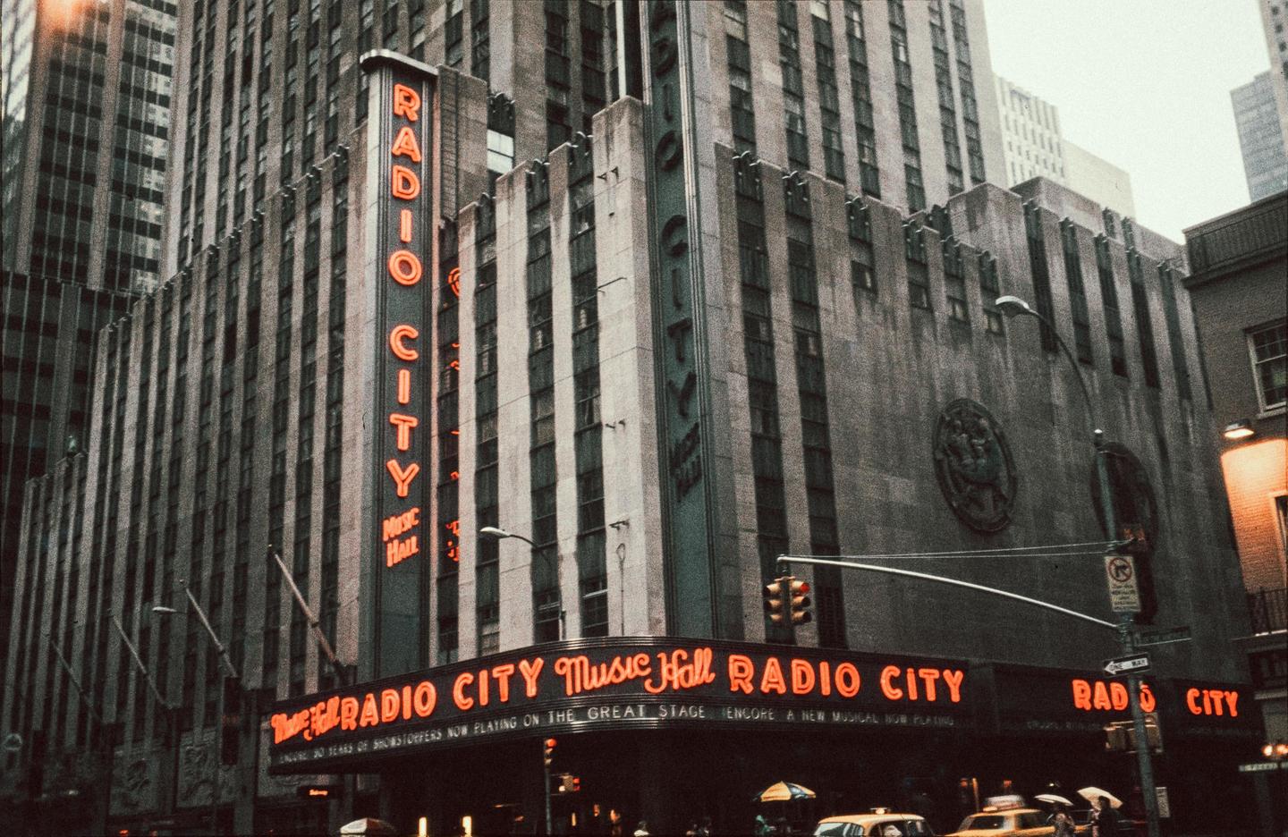 A large building with a prominent vertical sign that reads "RADIO CITY" in neon letters is shown from a low angle.