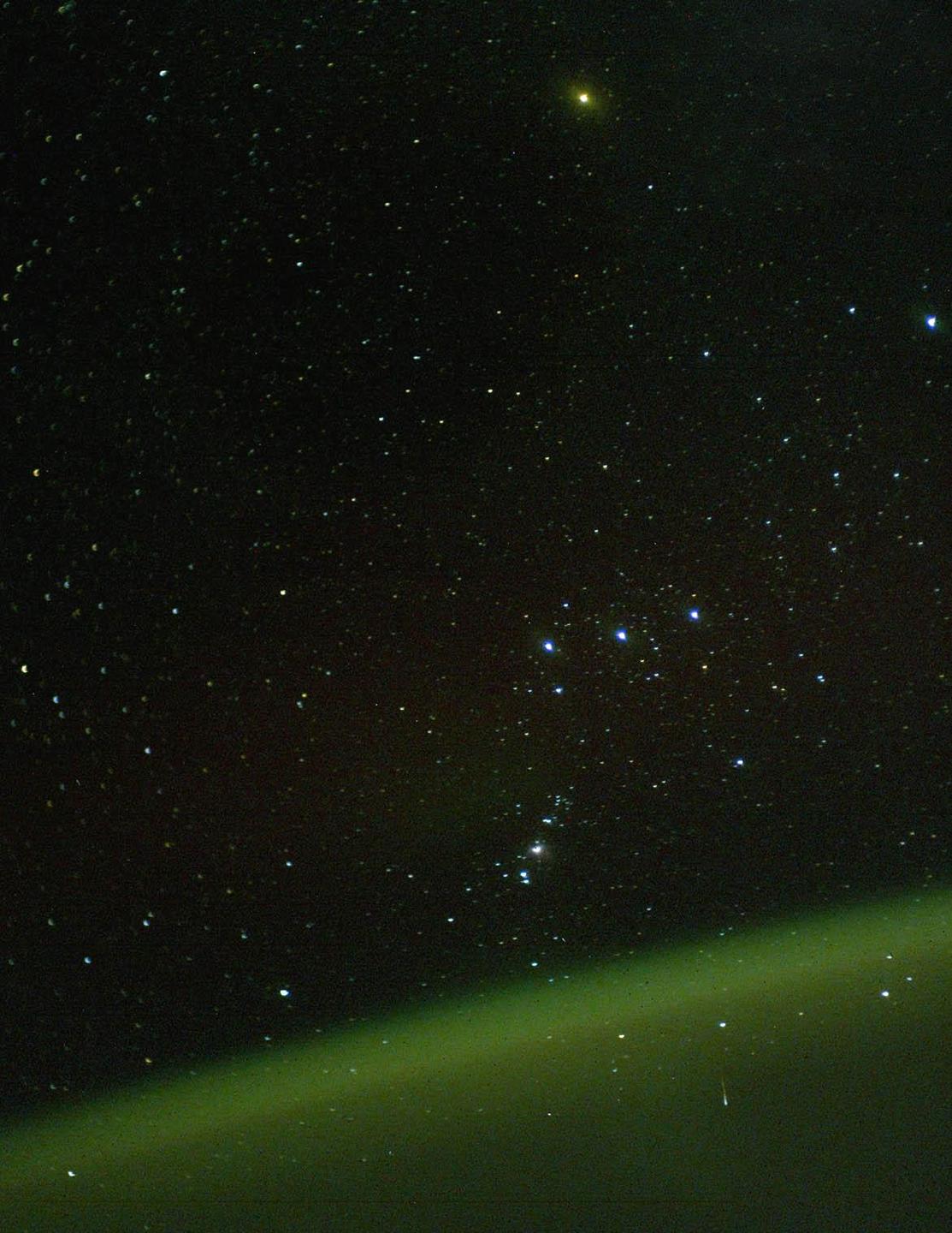 The Orion constellation is visible above a green atmospheric glow.