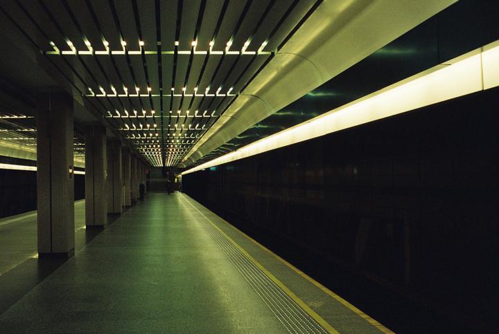 A long, empty subway platform is illuminated by overhead lights and a continuous strip light along the wall.