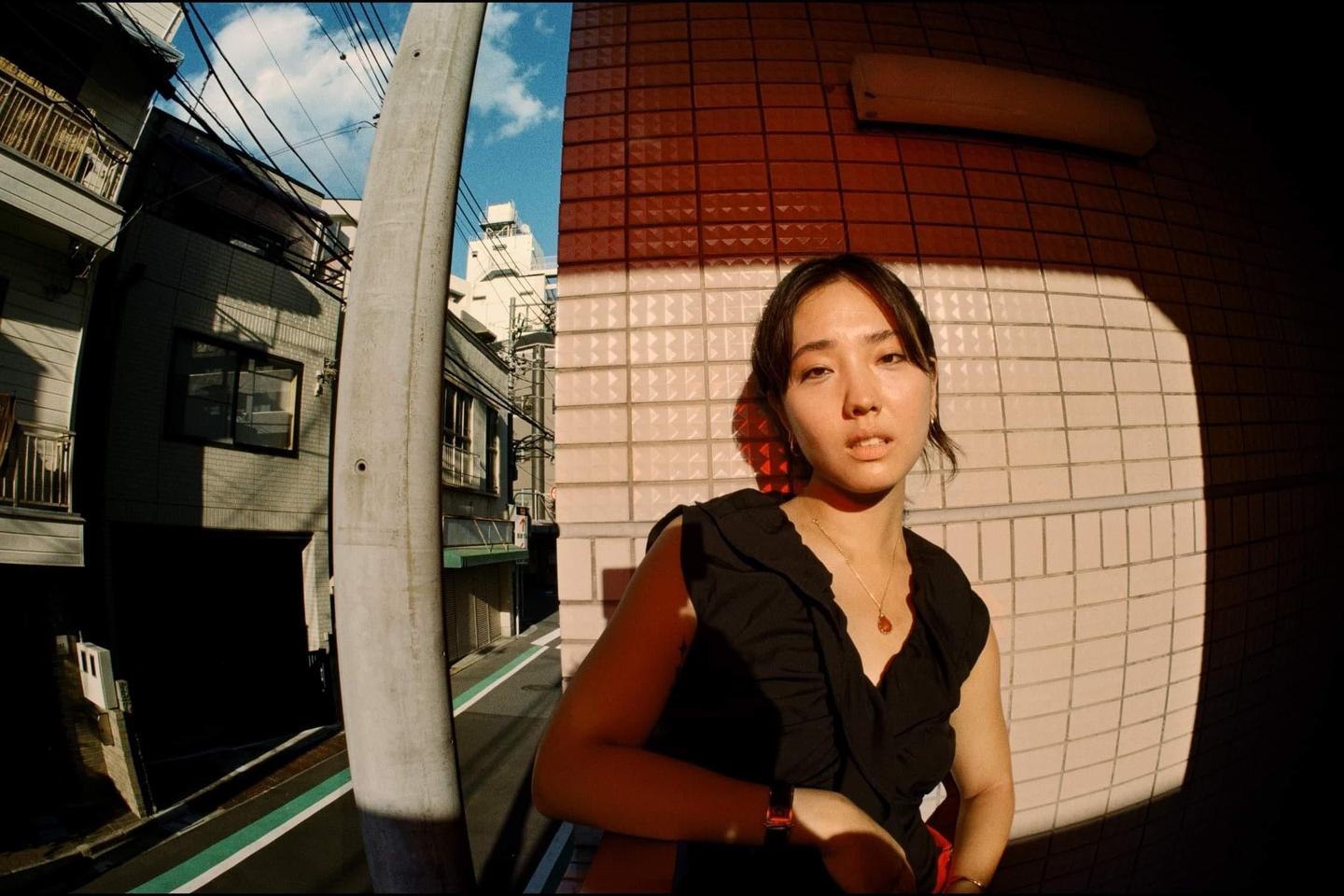 A woman stands in a narrow street with buildings and power lines in the background.